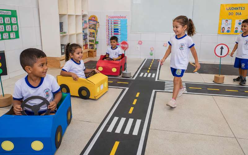 Crianças brincando de circuito de trânsito com faixas no chão simulando ruas e faixa de pedestre