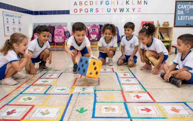 Crianças jogando trilha de desafios no chão da sala em atividade de gamificação na educação infantil